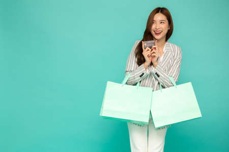 Portrait of smiling asian women holding credit card and green shopping bag isolated over green...