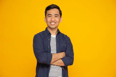 Portrait of asian man with arms crossed and smile isolated over yellow background, Looking at camera, Happy feeling conceptの写真素材