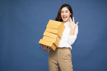 Happy Asian woman smiling and holding package parcel box isolated on deep blue background, Delivery courier and shipping service conceptの写真素材