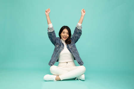 Attractive beautiful Asian woman sitting on floor and hands up raised arms from happiness isolated...