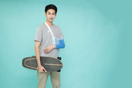 Young Asian man put on a soft splint due to a broken arm due to a skating accident isolated on green...
