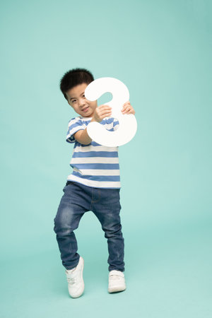 Asian boy showing number 3 or three isolated on green background, Full length people compositionの写真素材