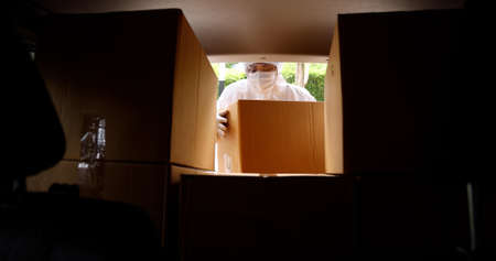 Woman in protective suits and masks unloading paper boxes with coronavirus vaccine from the carの写真素材