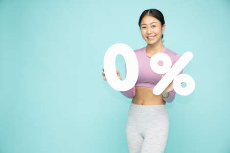 Young Asian woman wearing yoga or exercise clothes showing and holding 0% number or zero percent...