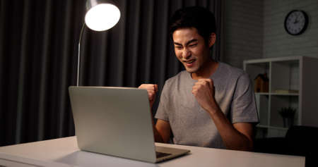 Attractive  young Asian man is very happy while working at home with laptop sitting alone at a desk...