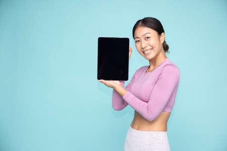 Portrait of Asian sporty woman showing or presenting tablet on hand isolated over green backgroundの写真素材