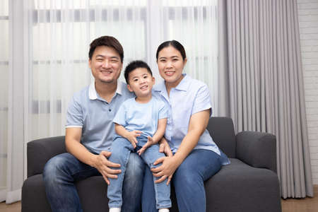 Happy Asian family with little son sitting on sofa together at home