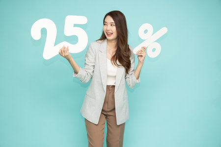 Asian business woman showing and holding 25% number or twenty five percent isolated over light green...