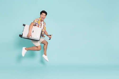 Happy Young Asian traveler man jumping with suitcase bag isolated on green background, Tourist in...