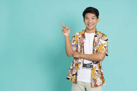 Happy cheerful young Asian man in summer shirt pointing to copyspace isolated on green backgroundの写真素材