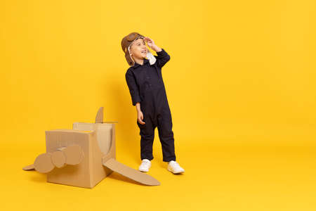 Asian little boy playing with cardboard airplane isolated on yellow backgroundの写真素材
