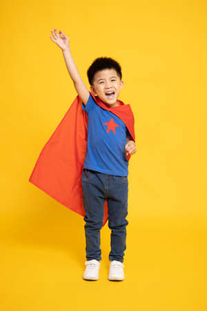 Smiling Superhero Asian boy in red cape isolated yellow background, Full body compositionの写真素材