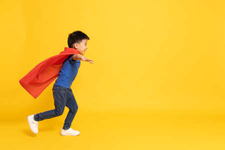 Superhero Asian boy in red cape running isolated yellow background, Full body compositionの写真素材