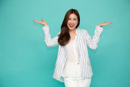 Happy Asian businesswoman in suit presenting or showing open hand palm with copy space for product isolated on green backgroundの写真素材