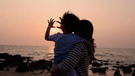 Silhouette of Happy family mother and son making heart shape by hand at sunset on the beach