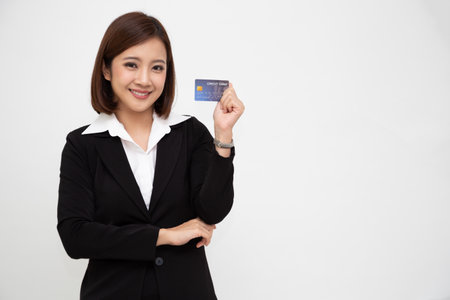 Young beautiful Asian business woman wearing black suit smiling, showing, presenting credit card for paying online business isolated on white backgroundの写真素材