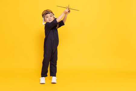 Asian little boy playing with cardboard airplane isolated on yellow backgroundの写真素材