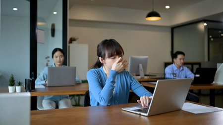 Young employee Asian woman is yawning at her work place with laptop computerの写真素材