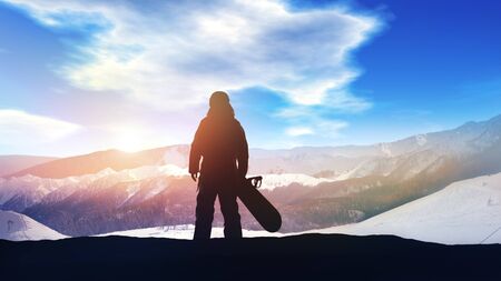 Silhouette of a snowboarder on a background of sunlit snowy mountains.の写真素材