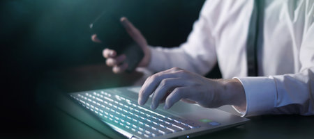Businessman with a smartphone works on laptop.