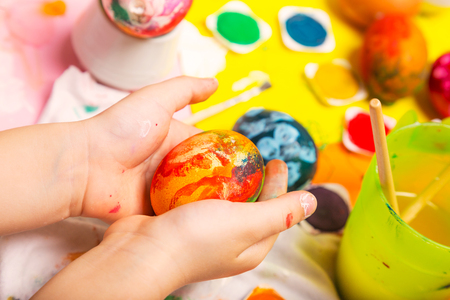 Colorful Easter painted egg in cildren hands hands over the work tableの写真素材