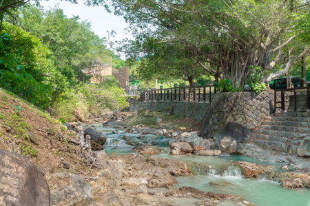 Beautiful nature river water from outdoor waterfall, slow flowing stream with rock and green tree in...