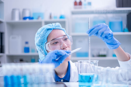Professional woman specialist doctor laboratory white uniform use thermometer temperature on blue liquid in healthcare and medicine experiment equipment with glove care, young adult female scientistの写真素材
