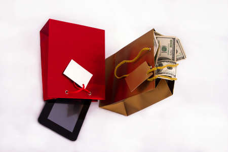 A red gift bag with a Tablet PC and a gold gift bag with dollars, isolated