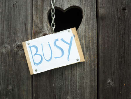 A close up view of a sign "Busy" hanging at a vintage wooden toilet doorの写真素材