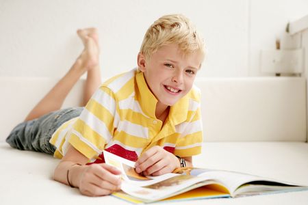 Close-up of a blond boy lying at the floor and looking smiling in a book