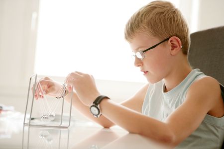 Close-up of a blond boy playing with a chrome pendulumの写真素材