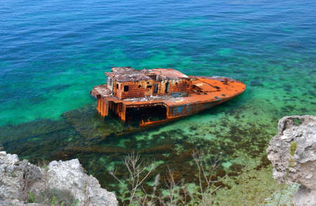Sunk ship in blue water, aground, near the coast の写真素材