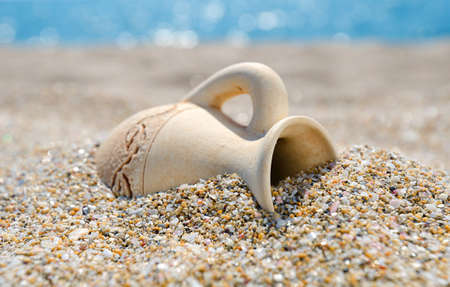 Ancient amphora in a sand on the beach against a blue seaの写真素材