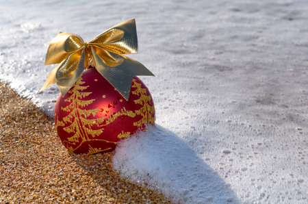 Christmas tree decoration on the beach sand in the foam of the sea waveの写真素材