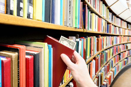 Reading/education makes you successful. Hand picking book with dollar bill in library