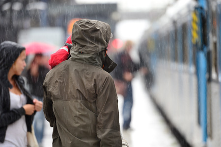 Man in raincoat in heavy rain on train station platformの写真素材
