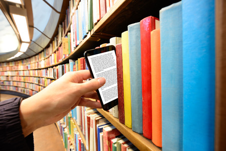 Hand picking a tablet computer out of bookshelf in libraryの写真素材