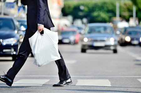 Man in suit with plastic bag crossing streetの写真素材