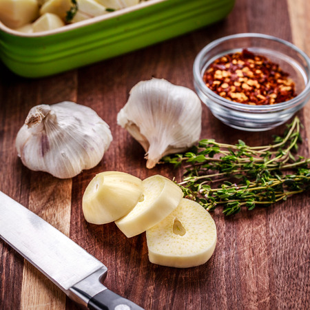 Preparing ingredients for roasted garlic, includes fresh thyme and crushed red pepper.   Chopped garlic in in a ceramic baking dish.  Knife and roasting pan also shown