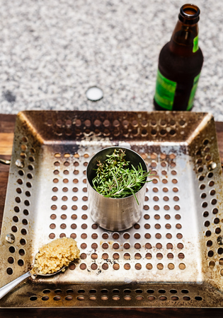 A beer can chicken grilling pan with rosemary and thyme in the cup.  A bottle of beer and a spoon of minced garlic also shown.の写真素材