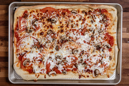 Over head photograph of a homemade red pizza that has been cooked with sliced tomato, bacon, and...