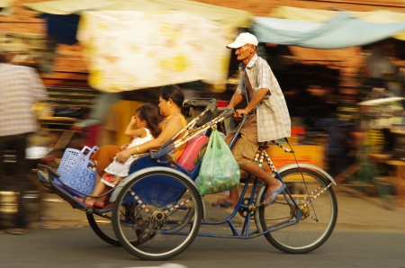 An old man driving his bicycle taxi with a woman and her child as passengersのeditorial素材