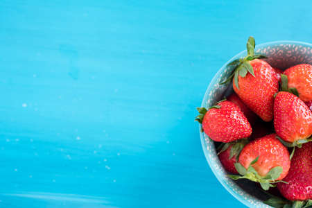 close view of somefresh strawberries in a bowl isolated on a blue backgroundの写真素材