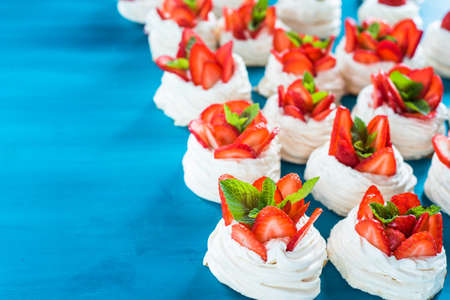 A small meringue Pavlova dessert with some strawberry slices with mint leaves on a blue backgroundの写真素材