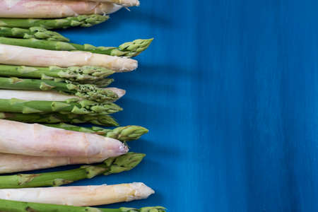 Bunches of green and white asparagus on a blue wooden background top viewの写真素材