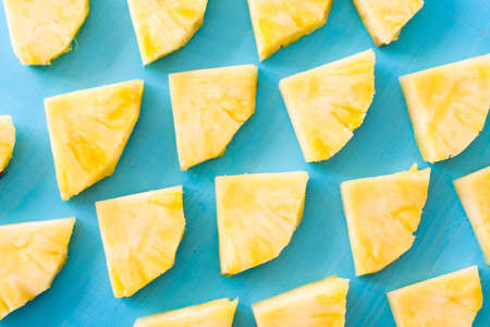 Spring or summer concept : Close up patter of many pieces of yellow pineapple laying on blue wooden table background.の写真素材