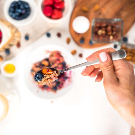 Top view showing hands eating porridge with honey nuts, blueberries on white wooden table selective focus, blurred background Good morning - healthy breakfast backgroundの写真素材