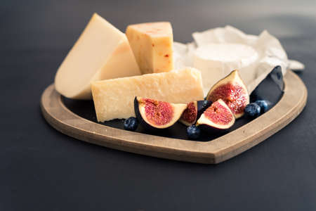 various types of cheese on rustic wooden table, goat cheese, chevre, grana padana, fig, blueberry