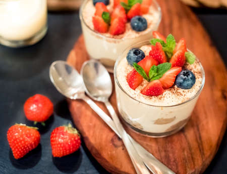 Homemade italian dessert tiramisu with strawberries, mint and blueberry in glassの写真素材