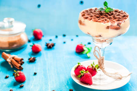 Summer dessert tiramisu, classic cheesecake with strawberries decorated with mint leaves. On a light blue wooden table, bright sunlight. Copy spaceの写真素材